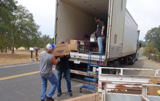 Tiger Paulk and Ronald Buckman carrying a heavy box of good supplies for the California Valley Miwok Tribe.