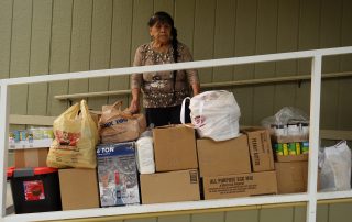 California Valley Miwok Tribal elder Mildred Burley standing with lots of donated good supplies.
