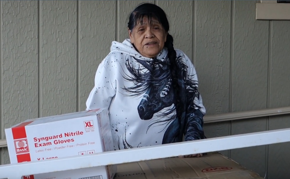 California Indian tribe elder Mildred Burley standing in front of boxes of supplies.