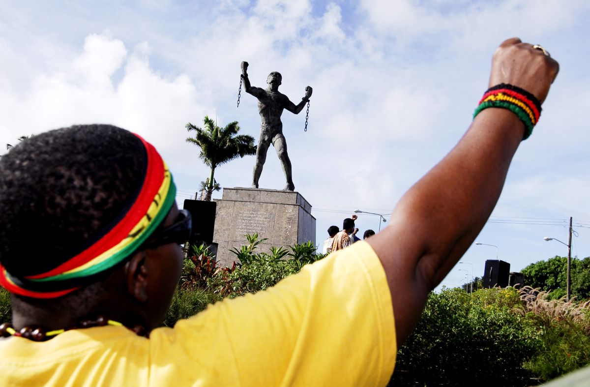 Barbadian person celebrating the Caribbean nation's annual Emancipation Day events by the statue of an enslaved African breaking the chains that held him.