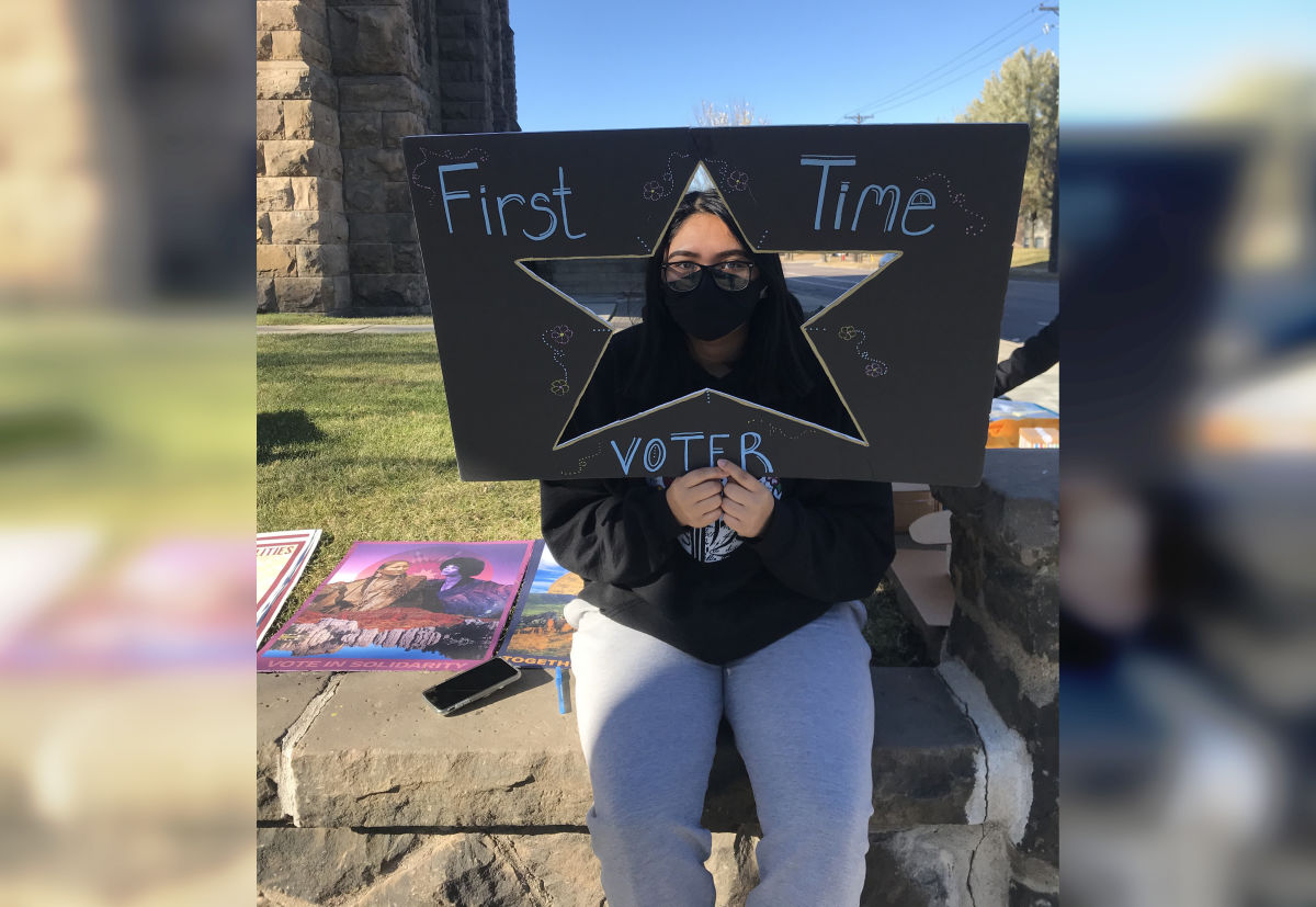 Native girl with black mask holding a sign saying "first time voter".