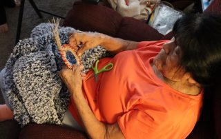 California Valley Miwok Tribal elder Mildred Burley, 87, sits on a couch with scissors, showcasing her artistry and strength in preserving her tribal culture.