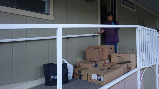 Mildred Burley stands with this month's donations that she will soon be providing to the local needy participant families as the Food for Tribal Families Director. Food for Tribal Families Director Mildred Burley looks towards a stack of packaged goods to be delivered to recipient families.
