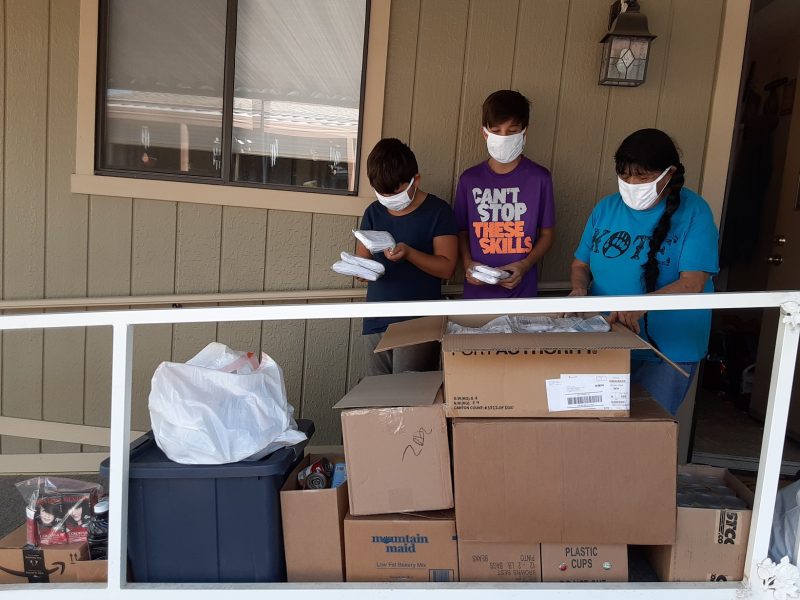 Program Director Mildred Burley seen here with tribal grandchildren D.J. and Dante,
looking through one box of Covid-19 supplies that will be dispersed to citizens families along with their allotments. August 2020 Food For Tribal Families Distribution
