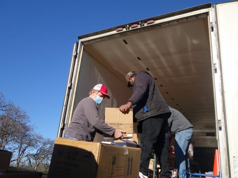 Specialist Ronald Buckman hands tribal staff another box as specialist Naz pulls more product down the conveyor.