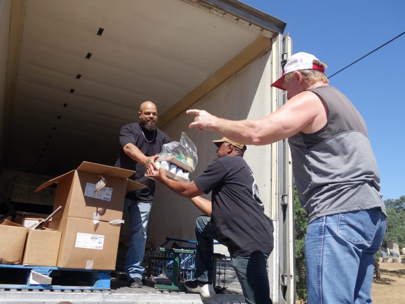 Tule River Food Distribution Specialist Naz carries on a conversation about current tribal events with tribal staff as Specialist Ronald Buckman accepts the last of one family's distribution. Tule River Food Distribution Specialists help California Valley Miwok Tribe staff Tiger Paulk unload good supplies.