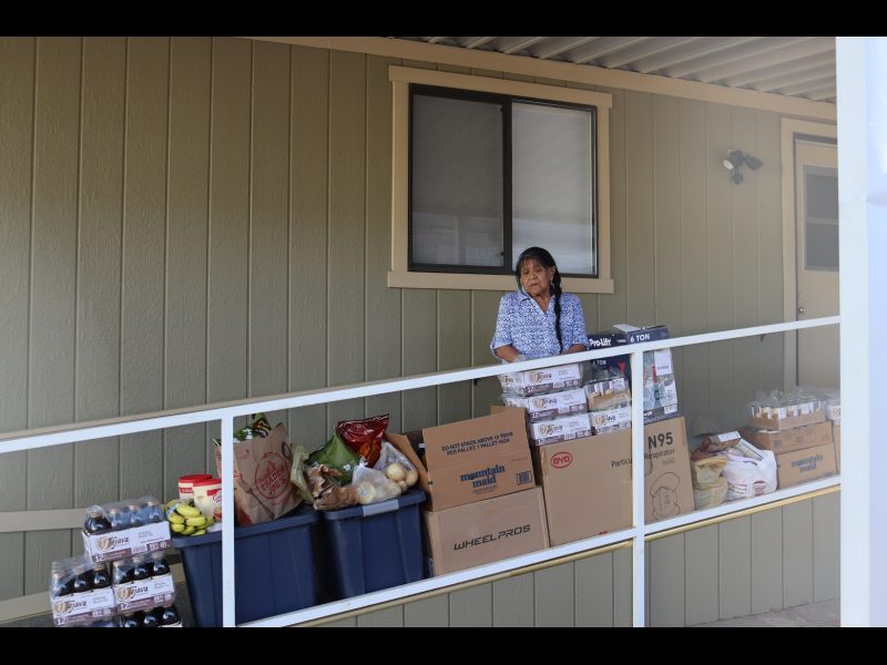 Additional view better shows all the extra included items and containers full of dry goods. California Indian tribe elder Mildred Burley standing in front of food supplies for the California Valley Miwok Tribe.