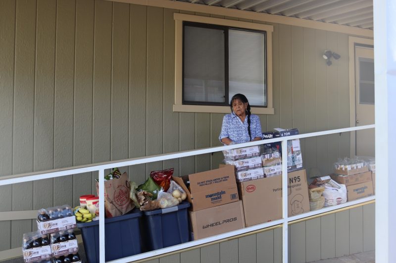 Additional view better shows all the extra included items and containers full of dry goods. California Indian tribe elder Mildred Burley standing in front of food supplies for the California Valley Miwok Tribe.