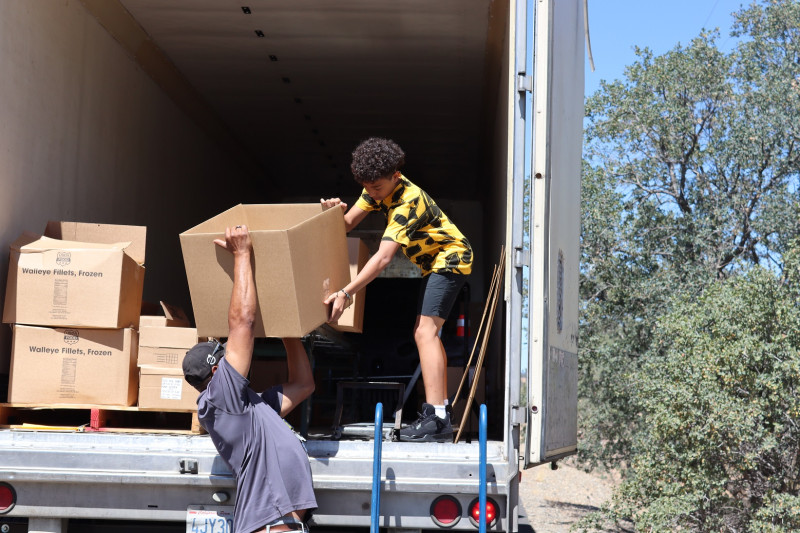 Here DuRon is handing down one of the many larger boxes of food to his father Ronald Buckman designated for recipient of the distribution. Duron Buckman and Ronald Buckman unloading food distributions for the California Valley Miwok Tribe