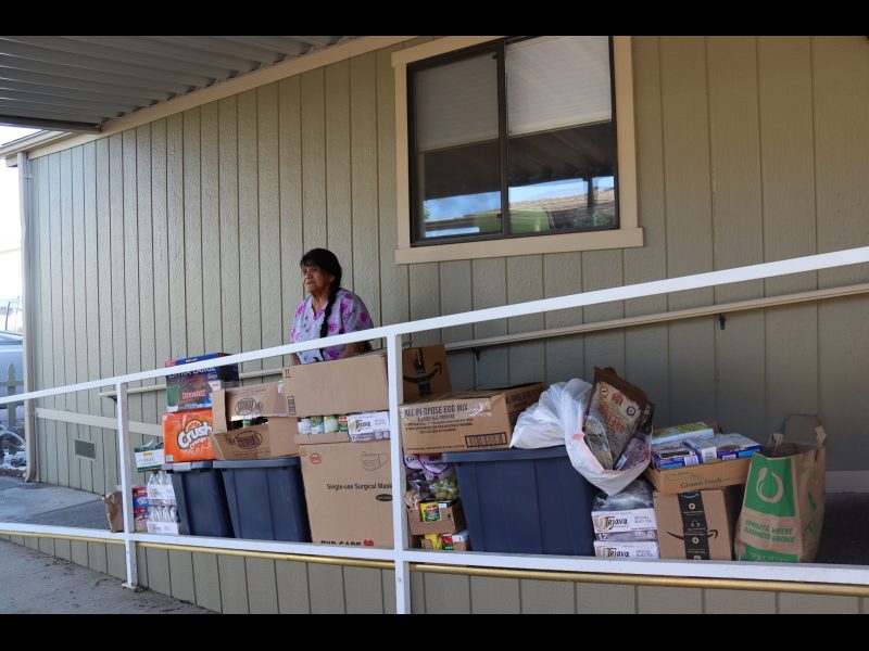 In this picture, Program Director Mildred Burley stands with food prior to video. California Valley Miwok Tribe elder Mildred Burley standing with goods deliveries.