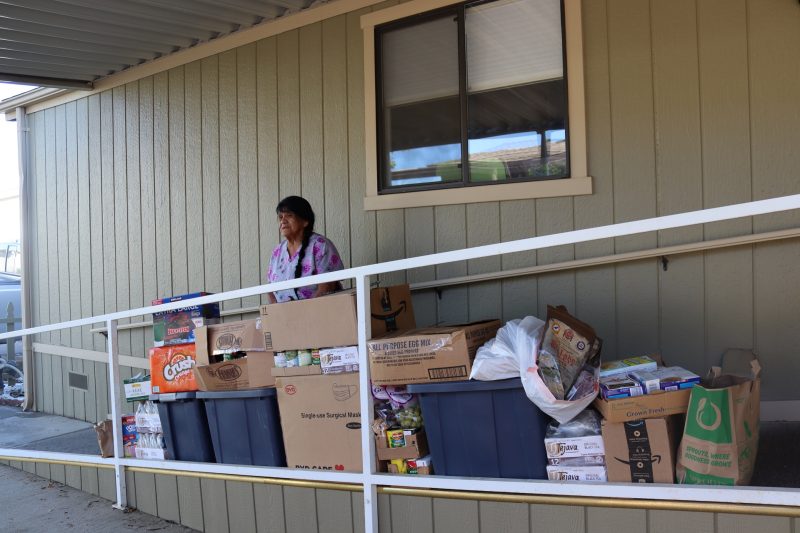 In this picture, Program Director Mildred Burley stands with food prior to video. California Valley Miwok Tribe elder Mildred Burley standing with goods deliveries.