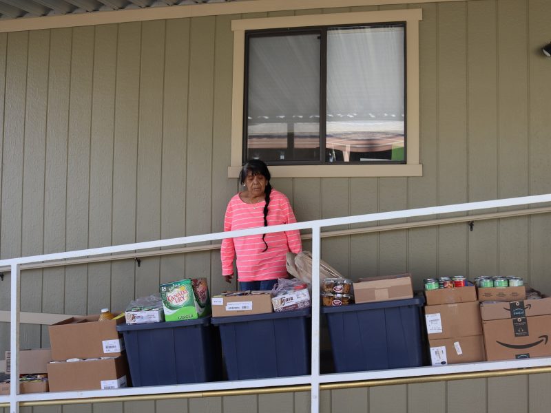 CVMT's tribal elder Mildred Burley standing in front of boxes of goods.