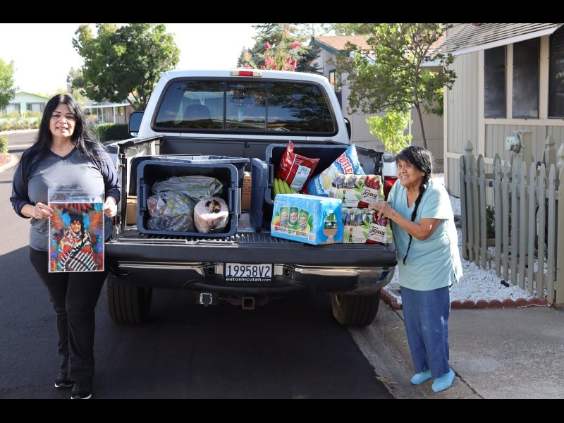Chairperson of the California Valley Miwok Tribe, (Silvia Burley) and Program Director for the Food For Tribal Families Program, (Mildred Burley).
Chairperson Burley stands holding a picture of Mildred in full regalia. Silvia and Mildred Burley in front of a truck filled with goods for Miwok tribe members.