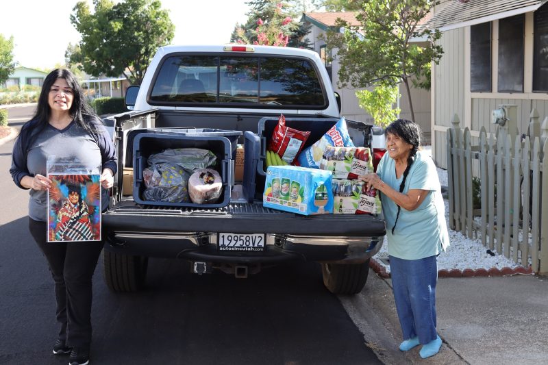 Chairperson of the California Valley Miwok Tribe, (Silvia Burley) and Program Director for the Food For Tribal Families Program, (Mildred Burley).
Chairperson Burley stands holding a picture of Mildred in full regalia. Silvia and Mildred Burley in front of a truck filled with goods for Miwok tribe members.