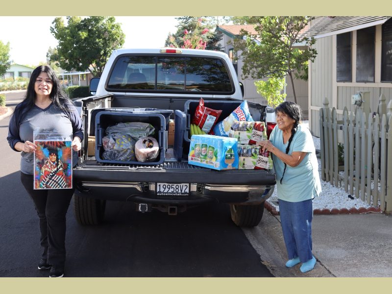 Chairperson of the California Valley Miwok Tribe, (Silvia Burley) and Program Director for the Food For Tribal Families Program, (Mildred Burley).
Chairperson Burley stands holding a picture of Mildred in full regalia. Silvia and Mildred Burley in front of a truck filled with goods for Miwok tribe members.
