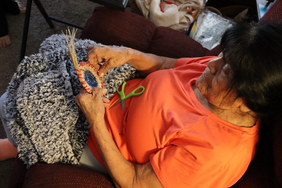 87 years young, tribal culture, artistry, language retention, Program Director Mildred Burley more native than anyone in the U.S. government or locally trying to kick her out of her tribe, can not even be conquered by crippling rheumatoid arthritis when weaving important items (culturally related) when asked upon from a tribal citizen. California Valley Miwok Tribal elder Mildred Burley, 87, sits on a couch with scissors, showcasing her artistry and strength in preserving her tribal culture.