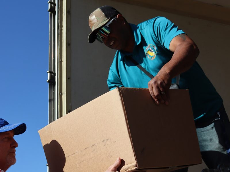 Ronald Buckman handing off part of distribution to tribal staff. Ronald Buckman hanging off goods to tribal member Tiger Paulk during the USDA food distribution in October 2024.