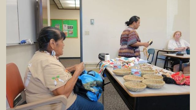 Here a university official is seen walking back to other attendees to share a traditional "rattle" "Tukal-al-y" that was brought as part of the presentation. It is made from deer bone with deer hoves attached by buckskin. Tribal Elder Mildred Burley also seen herenis explaining its significance and use during cultural dancing and singing.