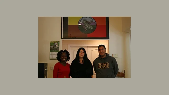 Standing below the tribal flag created from the Official Seal of the California Valley Miwok Tribe, are clockwise from left: Ms. Olushade Unger, Chairperson Silvia Burley and Mr. Aries Rivers Yumul.